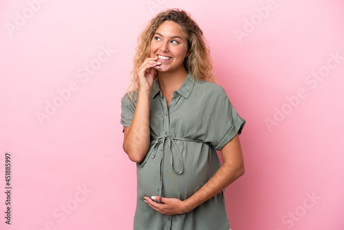 Girl with curly hair isolated on pink background pregnant and thinking