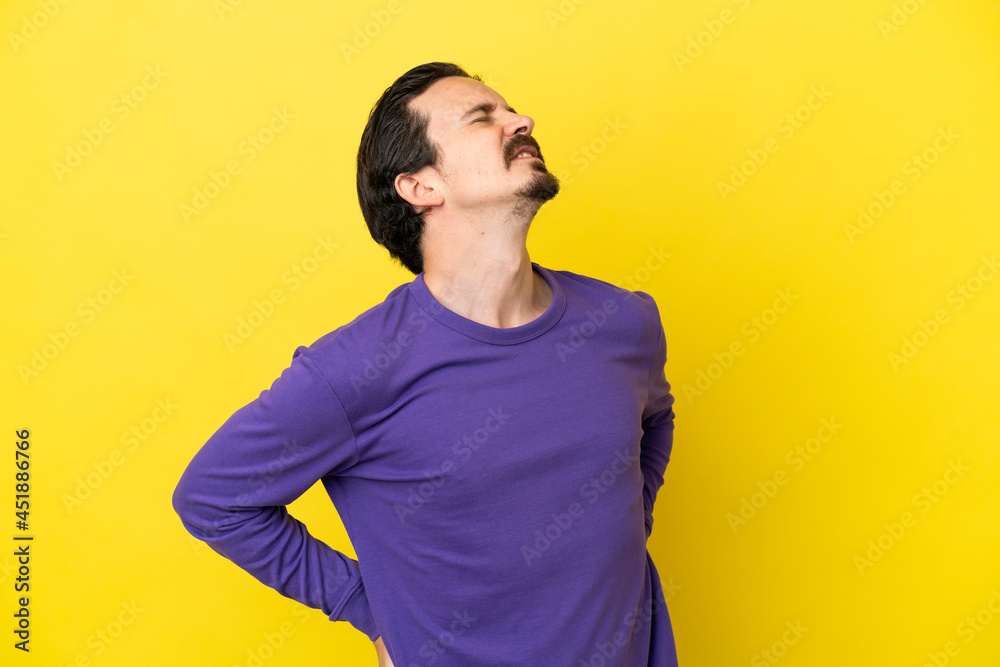Young caucasian man isolated on yellow background suffering from backache for having made an effort Young caucasian man isolated on yellow background suffering from backache for having made an effort