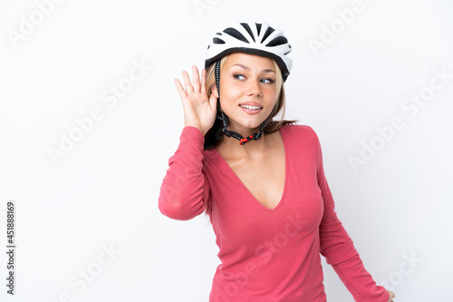 Young Russian woman wearing a bike helmet isolated on white background listening to something by putting hand on the ear