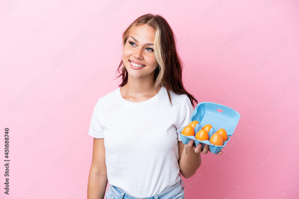 Young Russian woman holding eggs isolated on pink background looking side Young Russian woman holding eggs isolated on pink background looking side