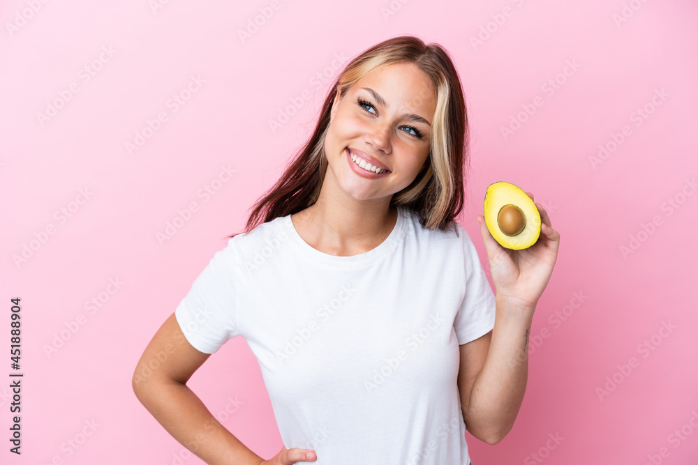 Young Russian woman holding avocado isolated on pink background posing with arms at hip and smiling Young Russian woman holding avocado isolated on pink background posing with arms at hip and smiling