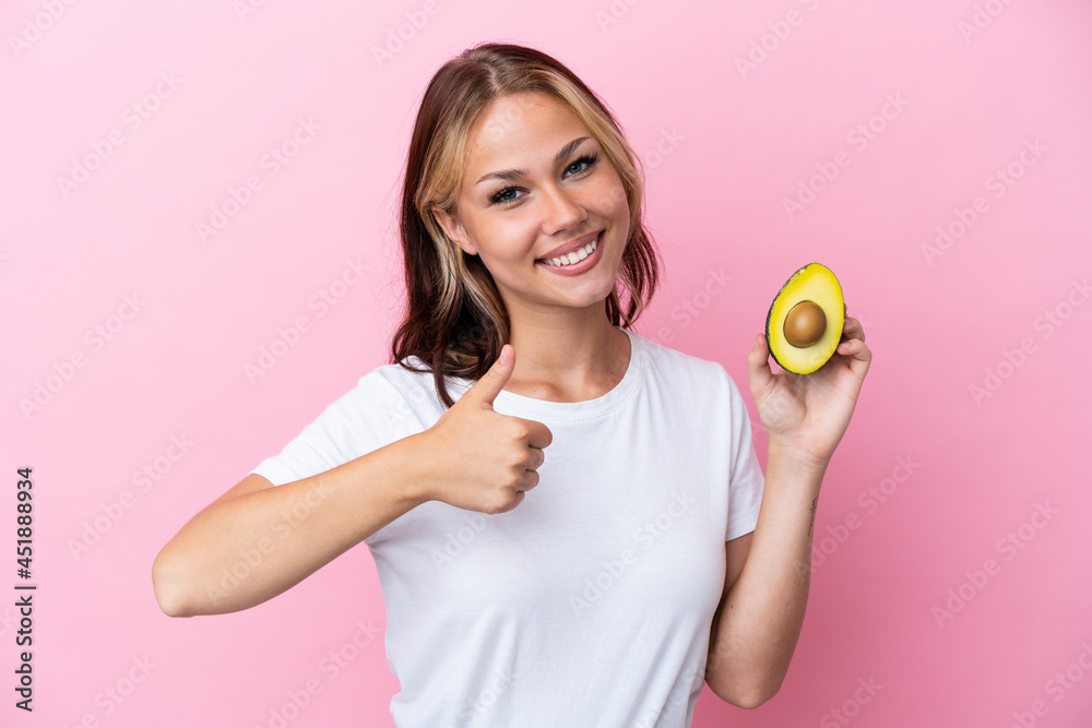 Young Russian woman holding avocado isolated on pink background giving a thumbs up gesture Young Russian woman holding avocado isolated on pink background giving a thumbs up gesture