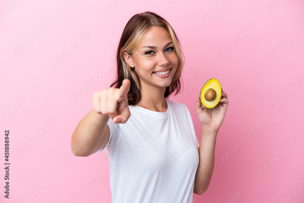 Young Russian woman holding avocado isolated on pink background pointing front with happy expression Young Russian woman holding avocado isolated on pink background pointing front with happy expression