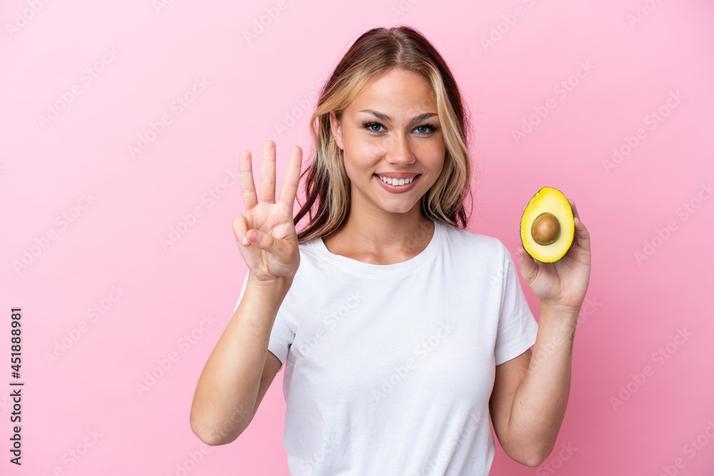 Young Russian woman holding avocado isolated on pink background happy and counting three with fingers Young Russian woman holding avocado isolated on pink background happy and counting three with fingers