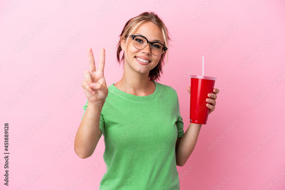 Young Russian woman holding a refreshment isolated on pink background smiling and showing victory sign Young Russian woman holding a refreshment isolated on pink background smiling and showing victory sign