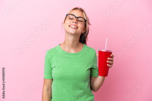Young Russian woman holding a refreshment isolated on pink background laughing