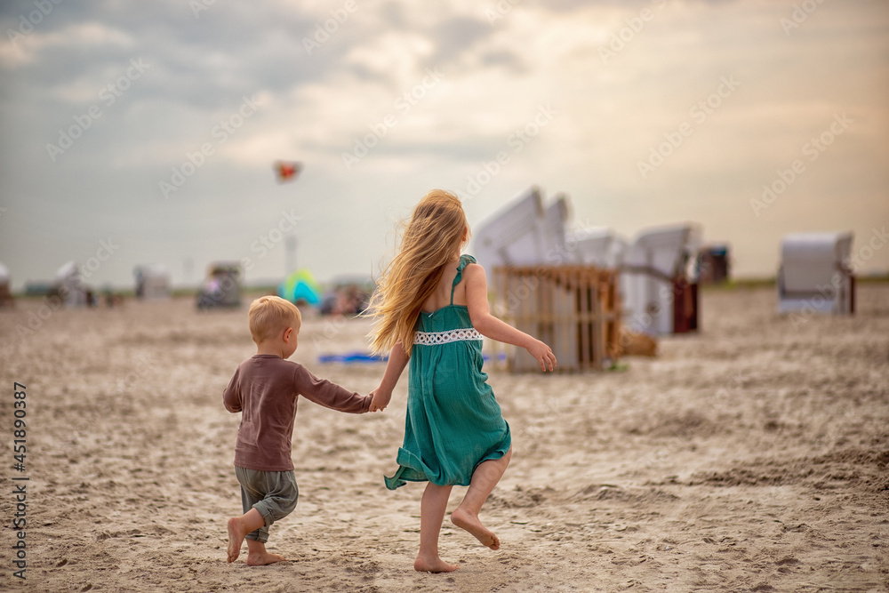 little boy and girl run in the summer along the seashore, holding hands. Brother and sister in natural clothes. Tourism, vacations, traveling with children, sun protection and safety.