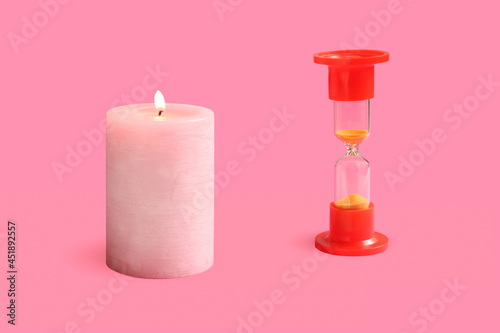 A burning pink candle and an hourglass on a pink background.