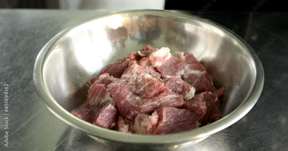 Adding some salt to pork meat. Chopped pieces of red meat are on the plates. Top view. Adding some salt to pork meat. Chopped pieces of red meat are on the plates. Top view.