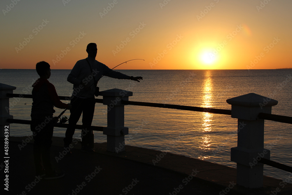 Fototapeta premium father and son fishing on the pier at sunset