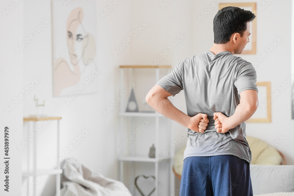 Fototapeta premium Young man suffering from back pain at home