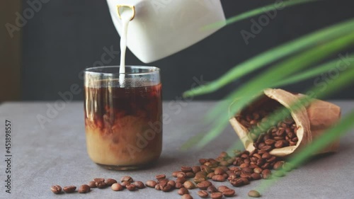 Milk cream is poured into a iced coffee. Coffee cold drink with ice and milk.
