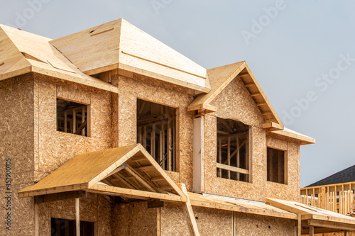 A residential frame house construction project showing the engineered truss roof rafters and oriented strand chip board engineered wall sheathing