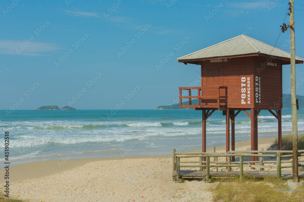 Wooden boardwalk on the beach with lifeguard tower on an empty beach with clear sand and blue sea in southern Brazil. Lifeguard station. Safety concept.