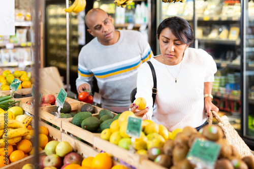 Positive hispanic couple choosing fresh foods in fruit and vegetable section of supermarket