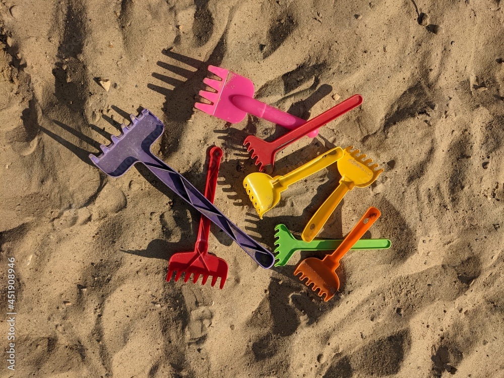 a bunch of multi-colored children's rakes in the sand. illustration for the proverb step on the same rake a bunch of multi-colored children's rakes in the sand. illustration for the proverb step on the same rake