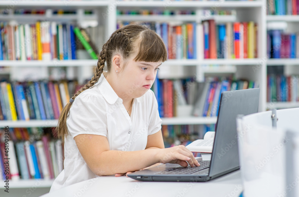 Smart young girl with syndrome down uses a laptop at school. Education for disabled children concept Smart young girl with syndrome down uses a laptop at school. Education for disabled children concept