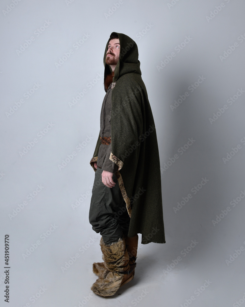 Full length  portrait of  young handsome man  wearing  medieval Celtic adventurer costume with hooded fur cloak, standing pose  isolated on studio background.