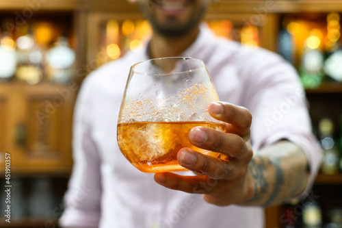 Male bartender serving whiskey in a clear crystal goblet.