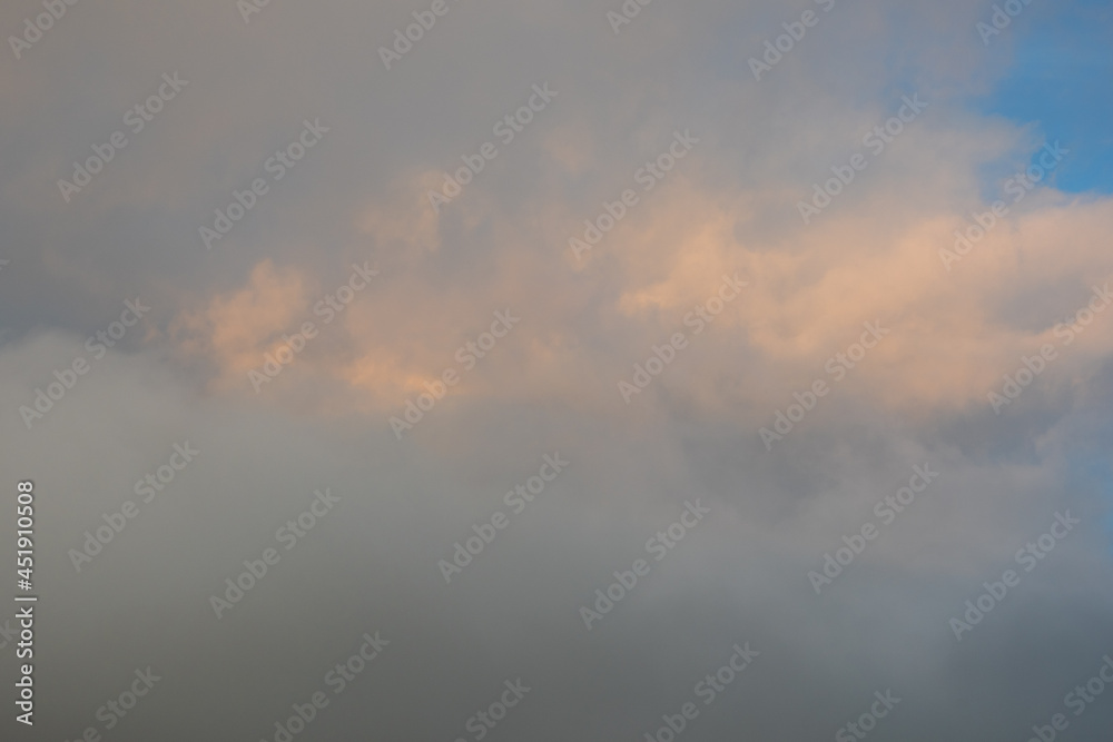 Blue-gray clouds in the sky illuminated by the setting sun. Light blue sky behind dark and dramatic storm clouds. Perfect natural sky background, mock up for design Blue-gray clouds in the sky illuminated by the setting sun. Light blue sky behind dark and dramatic storm clouds. Perfect natural sky background, mock up for design