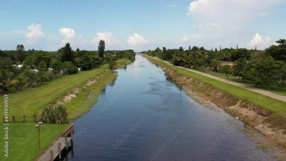 An aerial view of a long canal which stretches out to the horizon on a sunny day. The camera boom up near power lines over the waterway which cuts through the area with the blue skies above. An aerial view of a long canal which stretches out to the horizon on a sunny day. The camera boom up near power lines over the waterway which cuts through the area with the blue skies above.