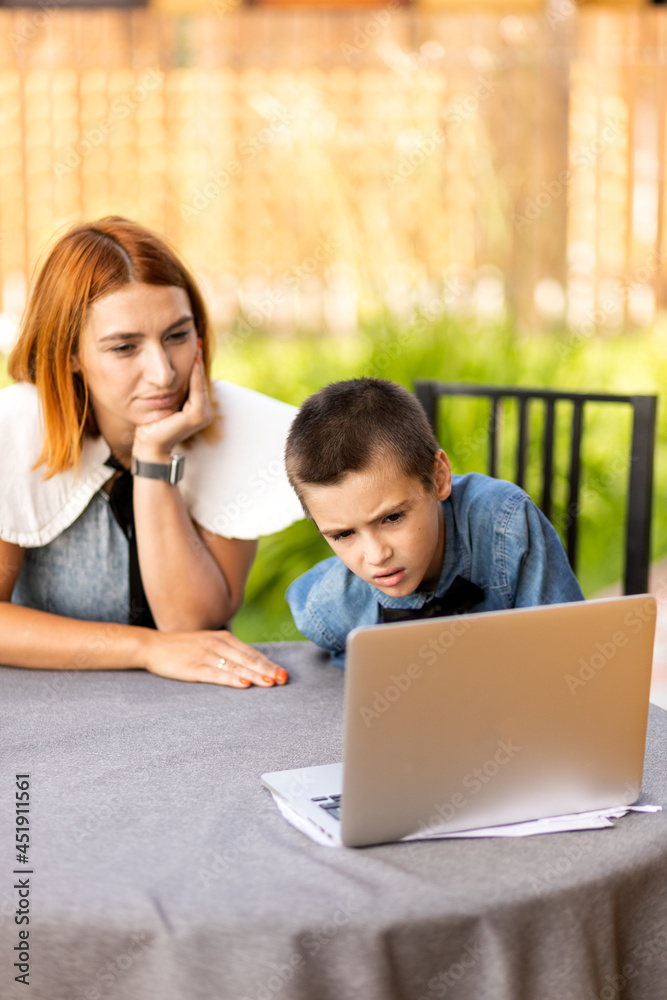 mom teaches the child at home in the garden, home schooling. Mom helps her son do his homework, stress. Online school lessons via laptop mom teaches the child at home in the garden, home schooling. Mom helps her son do his homework, stress. Online school lessons via laptop