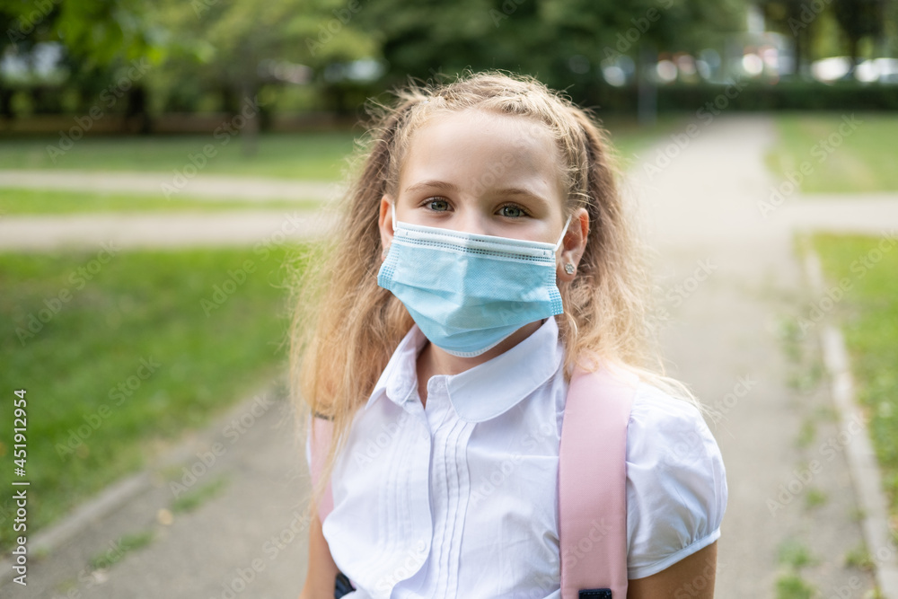 portrait of blonde curly schoolgirl in protective mask in school uniform with pink backpack back to school portrait of blonde curly schoolgirl in protective mask in school uniform with pink backpack back to school