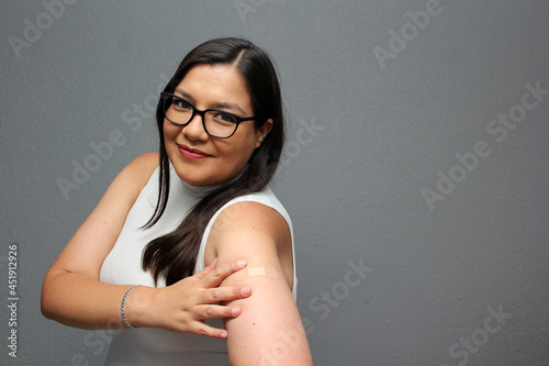Happy Latina adult woman shows her arm that just received the Covid-19 vaccine in the new normal for the coronavirus pandemic
 photo