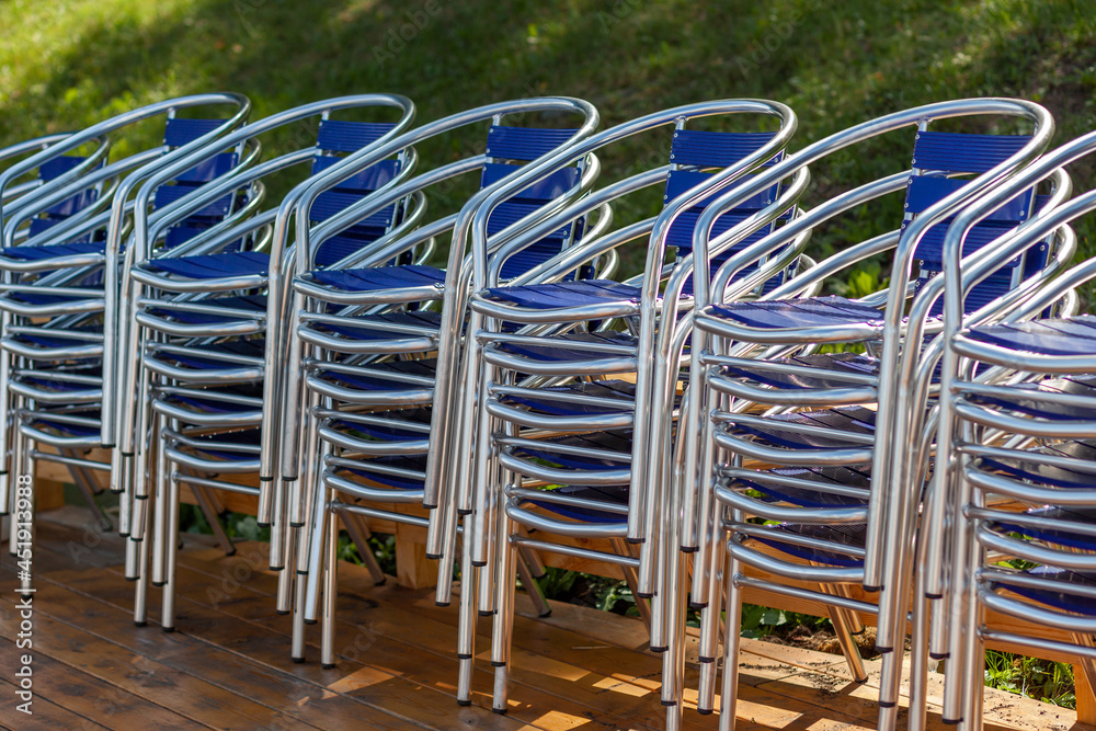 Metal chairs stacked in piles, and next to a beach umbrella in a street restaurant, cafe or recreation center. The chairs are on the wooden floor. Resorts are waiting for tourists and visitors