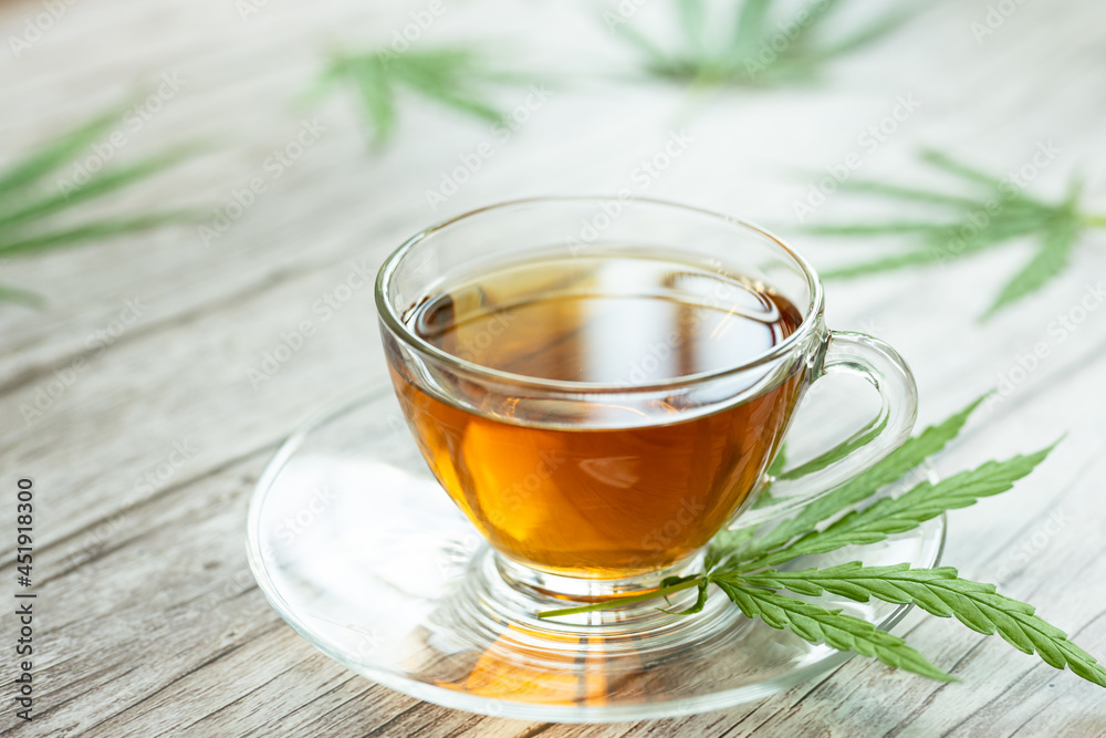 Glass cup of cannabis herbal tea. Cup of tea with marijuana and fresh green leaves on the wooden background. Glass cup of cannabis herbal tea. Cup of tea with marijuana and fresh green leaves on the wooden background.