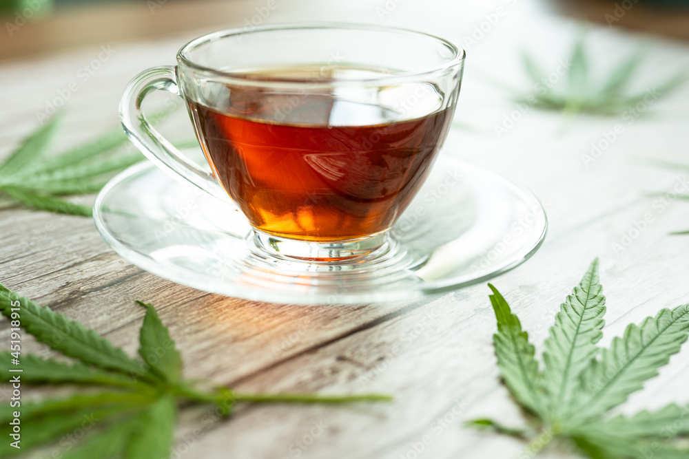 Glass cup of cannabis herbal tea. Cup of tea with marijuana and fresh green leaves on the wooden background. Glass cup of cannabis herbal tea. Cup of tea with marijuana and fresh green leaves on the wooden background.