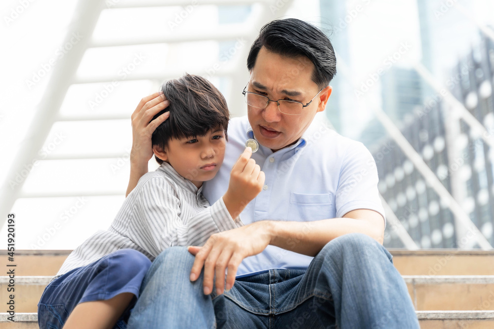 Father and son embracing each other with sad faces on the public corridor and his son's hand holding a coin That was the last money they had - Dad and son family concept Father and son embracing each other with sad faces on the public corridor and his son's hand holding a coin That was the last money they had - Dad and son family concept