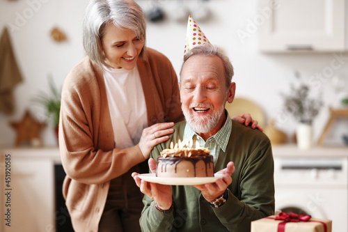 Happy elderly man in party hat holding chocolate cake with lit candles during Birthday celebration