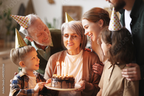 Happy senior woman holding cake with burning candles while celebrating birthday with big lovely family