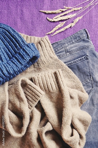 Blue wool hat, brown sweater and gray jeans on a purple background. Flat lay fall and winter fashion photography. Closeup detail clothes