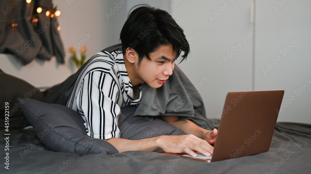Asian man surfing internet with computer laptop on bed at night. Asian man surfing internet with computer laptop on bed at night.
