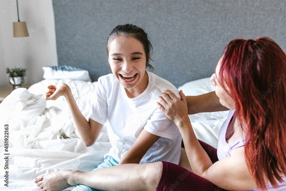 Latin mom and teenage daughter with cerebral palsy having fun on bed at home, in disability concept in Latin America