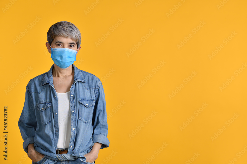 Happy middle aged Asian woman wearing surgical mask for corona virus isolated on yellow colour background