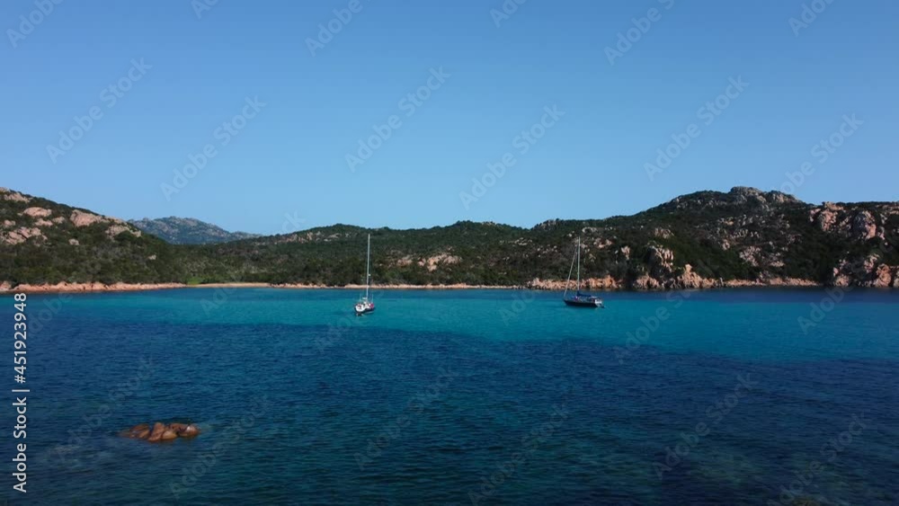 Sardinia holiday sailing ship boats in a beautiful Mediterranean rock beach seaside bay with crystal clear blue turquoise ocean water and little waves in Italy. Tourist vacation aerial drone above Sardinia holiday sailing ship boats in a beautiful Mediterranean rock beach seaside bay with crystal clear blue turquoise ocean water and little waves in Italy. Tourist vacation aerial drone above