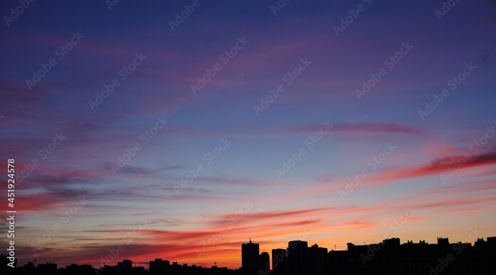 Colorful dramatic sky with clouds at sunset. City during warm sunset