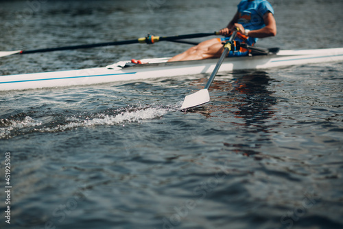 Sportsman single scull man rower rowing on boat. Oar paddle water splash movement