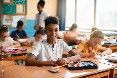 Happy black elementary student has class at school and looking at camera.