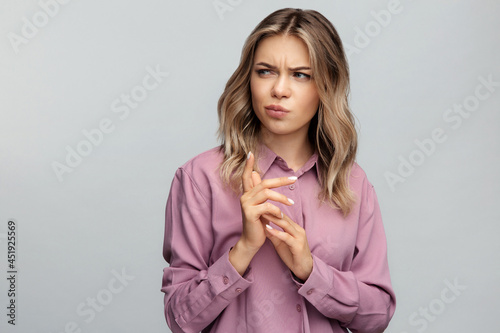 Confused young woman looking aside with skeptical and suspicious emotion thoughtful and pensive bending fingers while making decision. Portrait of sarcastic doubtful female isolated at studio wall