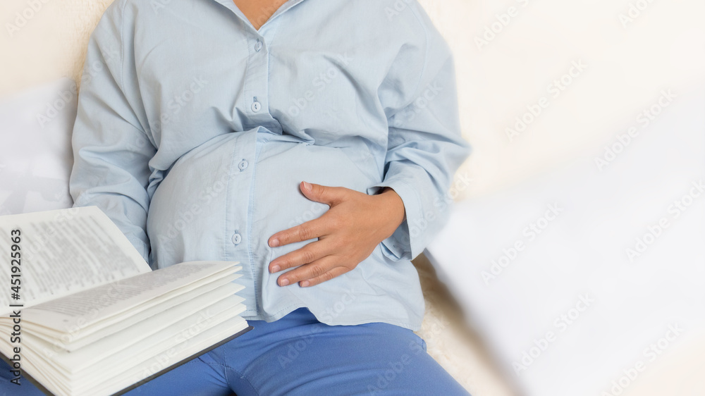 Preparing for fatherhood. A young pregnant woman is reading a book about childcare while holding one hand on her belly. Close-up. Depersonalization. Copy spase.
