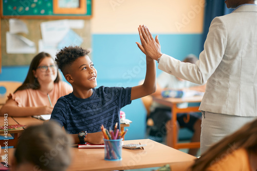 Fotografija Happy black elementary student and his teacher greet with high five gesture during class at school