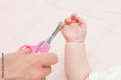 Mom gets a manicure with nail scissors and cuts her cute baby s nails while lying on the bed. The concept of child care.