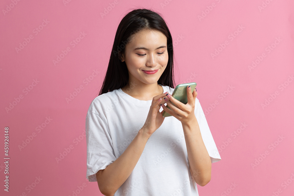 Smiling asian woman is pointing on smartphone standing on pink background Smiling asian woman is pointing on smartphone standing on pink background