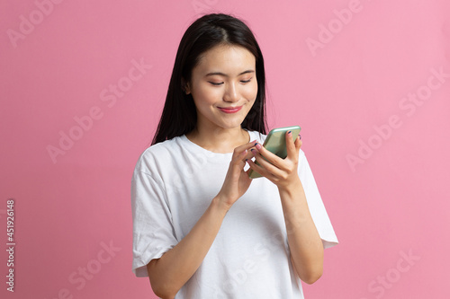 Fotografie Smiling asian woman is pointing on smartphone standing on pink background