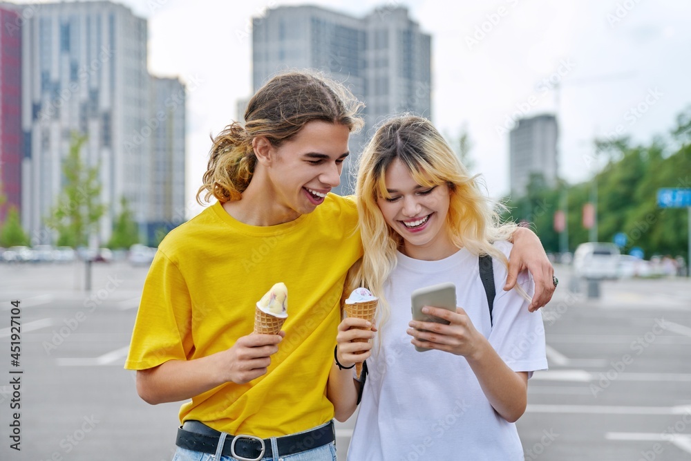 Happy laughing couple of teenagers walking hugging together in city