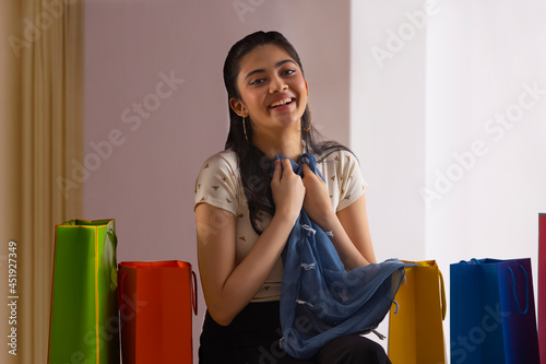 Wall Mural A young woman sitting amidst colorful shoppingbags  holding her new unpacked dress with delight